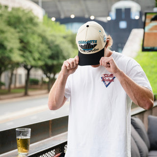 A person adjusts their Charlotte Snapback - The Kuechly, featuring a vintage skyline design, evoking a retro Panthers game day vibe.