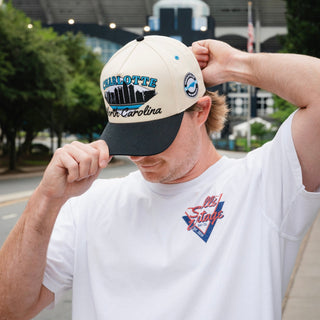 Person wearing the Charlotte Snapback - The Kuechly, featuring a retro CHARLOTTE North Carolina skyline design, reminiscent of early Carolina Panthers games.