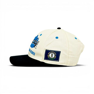 Kentucky Snapback - The Rupp: Cream crown with blue splatters, Kentucky script, state seal patch; black bill. Celebrates Kentucky basketball legacy.