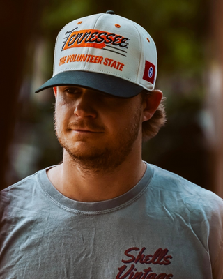 Young man wearing the Tennessee Snapback - The Neyland (Cream/Black) with a retro Tennessee logo, celebrating the legacy of Neyland Stadium in a vintage style.