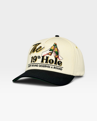 Retro-style snapback hat with a beige crown and black bill, featuring a golf-themed design: clinking beer bottles and The 19th Hole text, celebrating post-golf camaraderie.